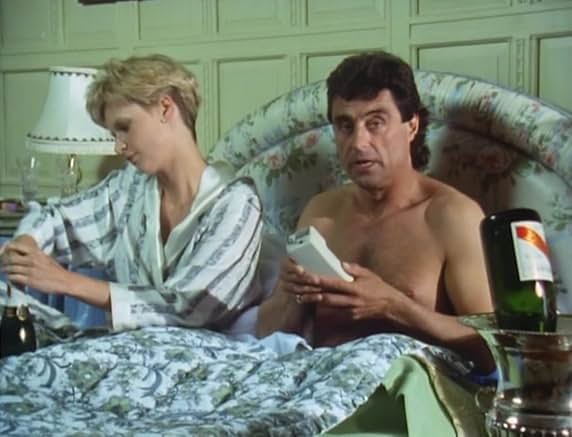 Lovejoy sitting up in a chintz four-poster with Melanie Ford, a bottle of champagne on ice beside them